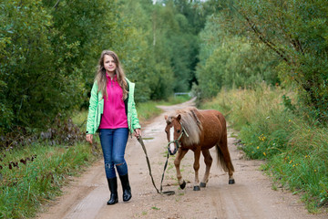 Teenage girl walking with a pony colt on a leash along a country road