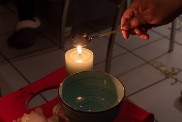 Hand beim Wachsgie&szlig;en mit Kerze, L&ouml;ffel und Schale mit Wasser