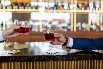 Two men in classic suits were drinking whiskey or cognac at the bar in the bar. Two young businessmen clink glasses of expensive alcoholic drink together, sitting in a pub