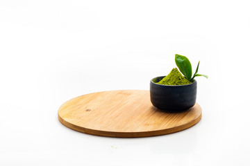 Isolate Heap Green Tea Powder in black ceramic bowl. Extract Tea Leaves in dark stone cup. With Mini green tea leaves on blank wooden plate.
