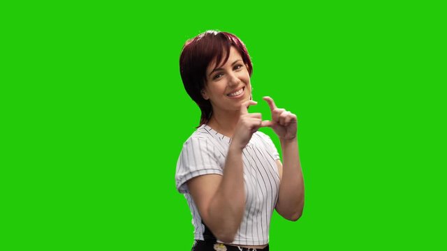 Beautiful smiling woman pose on green screen and make heart gesture with hands