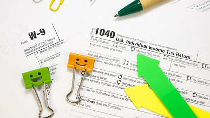 Smile Orange and Green Binder Clips with Pen on 1040 Tax Form and W-9. Individual Income Tax Return. Filing Taxes Document on Table in Office Concept