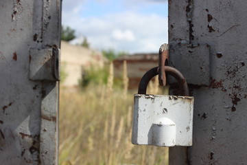 Old padlock on opened metal doors on blurred grass and abandoned building background on sunny summer day
