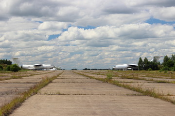 Abandoned concrete landing field with old soviet airplanes on horizon on cloudy sky background on Sunny summer day