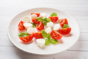 Caprese salad of tomatoes, mozzarella cheese and Basil on a white plate. Italian cuisine.