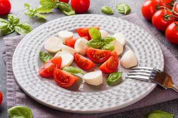 Caprese salad of tomatoes, mozzarella cheese and Basil on a dark background. Italian cuisine.