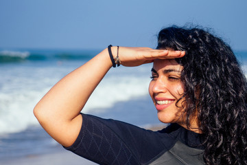 indian girl put her hand to forehead to shield her eyes from the sun looks away in Goa India beach