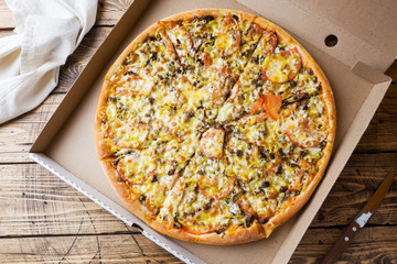 Freshly baked pizza in a cardboard box on a wooden table.