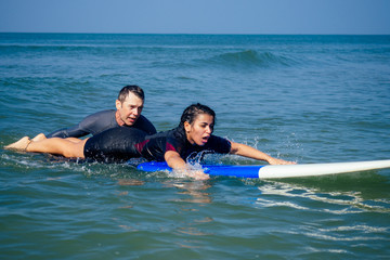 man instructor demonstrating how to paddle in the water by hands on surfboard to indian woman in...