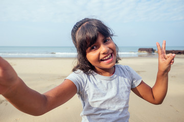 cute girl 7 or 8 years old Asian American mixed enjoying holidays taking selfie in Goa and soving V-sign victory