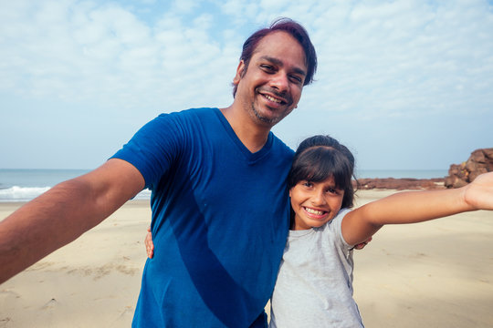 Smiling indian father and child taking selfie together looking at camera, head shot portrait of happy african family dad with kid embracing recording video in Goa