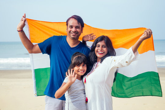 Happy Indian family holding national tricolour flag on beach Goa
