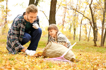 Man and his little daughter cleaning up autumn leaves outdoors