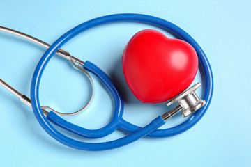 Modern stethoscope and red heart on color background