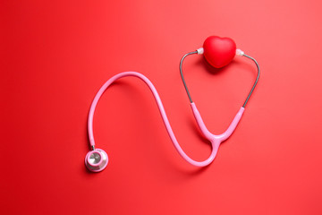 Modern stethoscope and red heart on color background