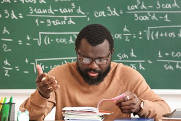 Displeased African-American teacher checking homework in classroom
