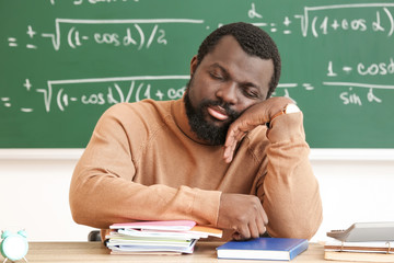 African-American teacher sleeping at table in classroom