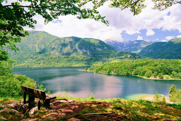 Bench at Bohinj Lake in Slovenia. Nature in Slovenija. Scenery view of green forest and blue water. Beautiful landscape in summer. Alpine Travel destination. Julian Alps mountains on scenic background