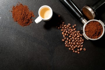 Coffee ground, beans and portafilter filter holder on black stone surface