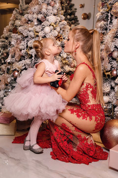 beautiful woman with blond hair in elegant dress  posing with cute daughter in decorated room with Christmas tree