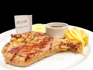 T-bone pork steak with french fries, pineapple slice and pepper sauce with steak knife and fork on white ceramic plate isolate on black background and make with paths.