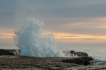 Waves crashing against rocks with sunrise in the background