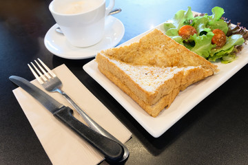 breakfast set serve on table, hot cappuccino coffee in white ceramic glass with tasty whole wheat bread sandwich ham cheese and salad vegetable. healthy food for start the day in the morning. 