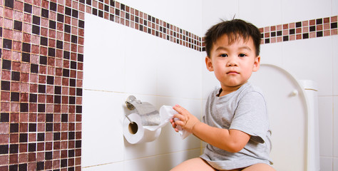 Asian little  kid 2-3 years old sitting on a kid bathroom accessory toilet