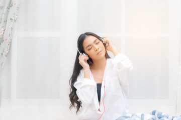 Beautiful young asian woman relaxing listening to music by white headphone in bedroom.