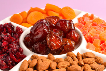 Mix of dried fruits and nuts on a white plate. Apricot, almond, raisin, dates fruit. On a lilac background. Space for text or design.