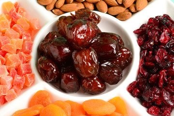 Mix of dried fruits and nuts on a white plate. Apricot, almond, raisin, dates fruit. On a brown background. Space for text or design.