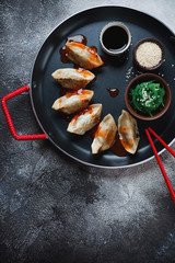 Serving pan with gyoza dumplings over dark-grey stone background, vertical shot with space, top view