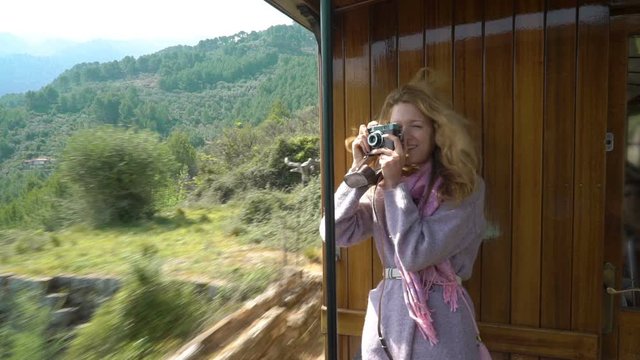 A young woman enjoying traveling on an old train, taking pictures of beautiful tourist locations using vintage camera, feeling excited and happy
