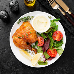 Baked chicken leg, served with sauce and fresh green salad. Black background