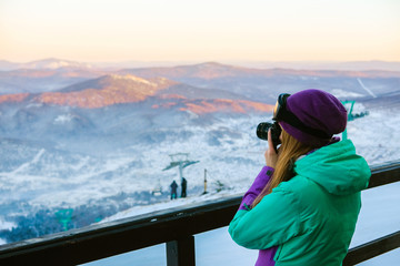 A woman photographs a winter landscape in the mountains.