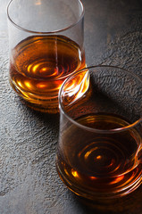 Cognac or Bourbon or rum in glass glasses on a dark brown background.