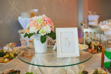 Decoration of the guest table with a sign 5 and flowers in a white vase