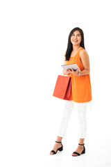 A beautiful Asian young woman wearing orange dress holding shopping bag and a tablet in front of white isolated background.