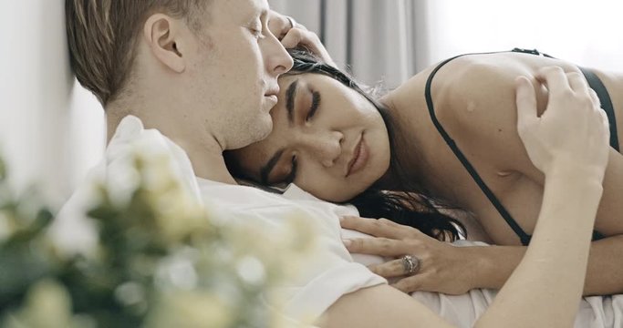Close up of woman laying on top of man in bed. Caucasian male with his girlfriend, asian woman in black lingerie. Happy lover in bed concept.