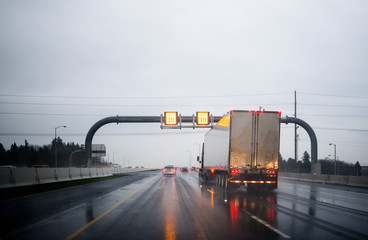 Big rig classic industrial semi truck transporting cargo in semi trailer driving on wet rainy...