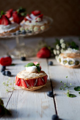 Delicate and rustic mini pavlova cakes with fresh strawberry and blueberry. 