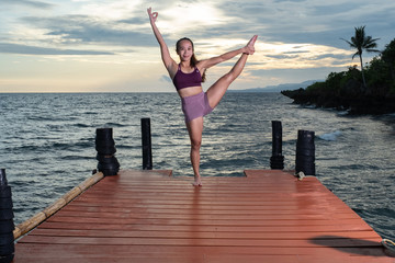 Young beautiful Filipina woman at tropical resort yoga and beauty posing poolside and oceansideat sunset in swimwear and athletic wear