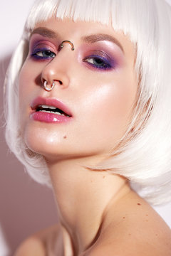 Young girl in the image of a fantasy with a piercing. Beautiful model in a white wig with bob and bright makeup. Beauty face. Shining skin. The portrait was taken in the studio.
