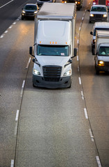 Big rig white bonnet semi truck with black grille transporting cargo in semi trailer running on...