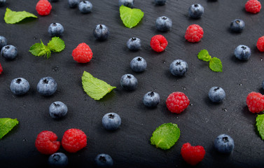 Ripe bilberry and raspberry berries on slate stone tray closeup
