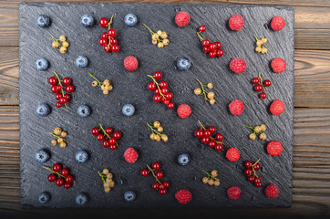 Flat lay view at ripe bilberry raspberry white and red currant on slate stone tray closeup