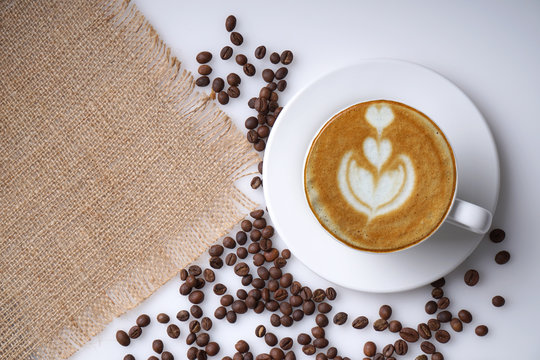 An image showing cup of coffee latte art and coffee beans on jute with space for text