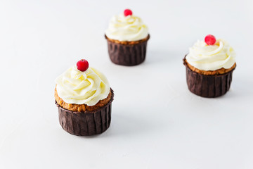 Carrot cupcakes with cream and cranberries on a white table. 