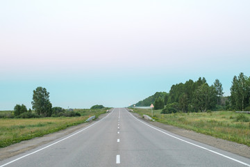 the road goes into the distance in the fog on the horizon on the sides of the grass grows and road signs during sunset
