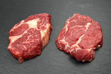 Two fresh raw marble meat, black Angus ribeye steak with spices on a dark stone background.